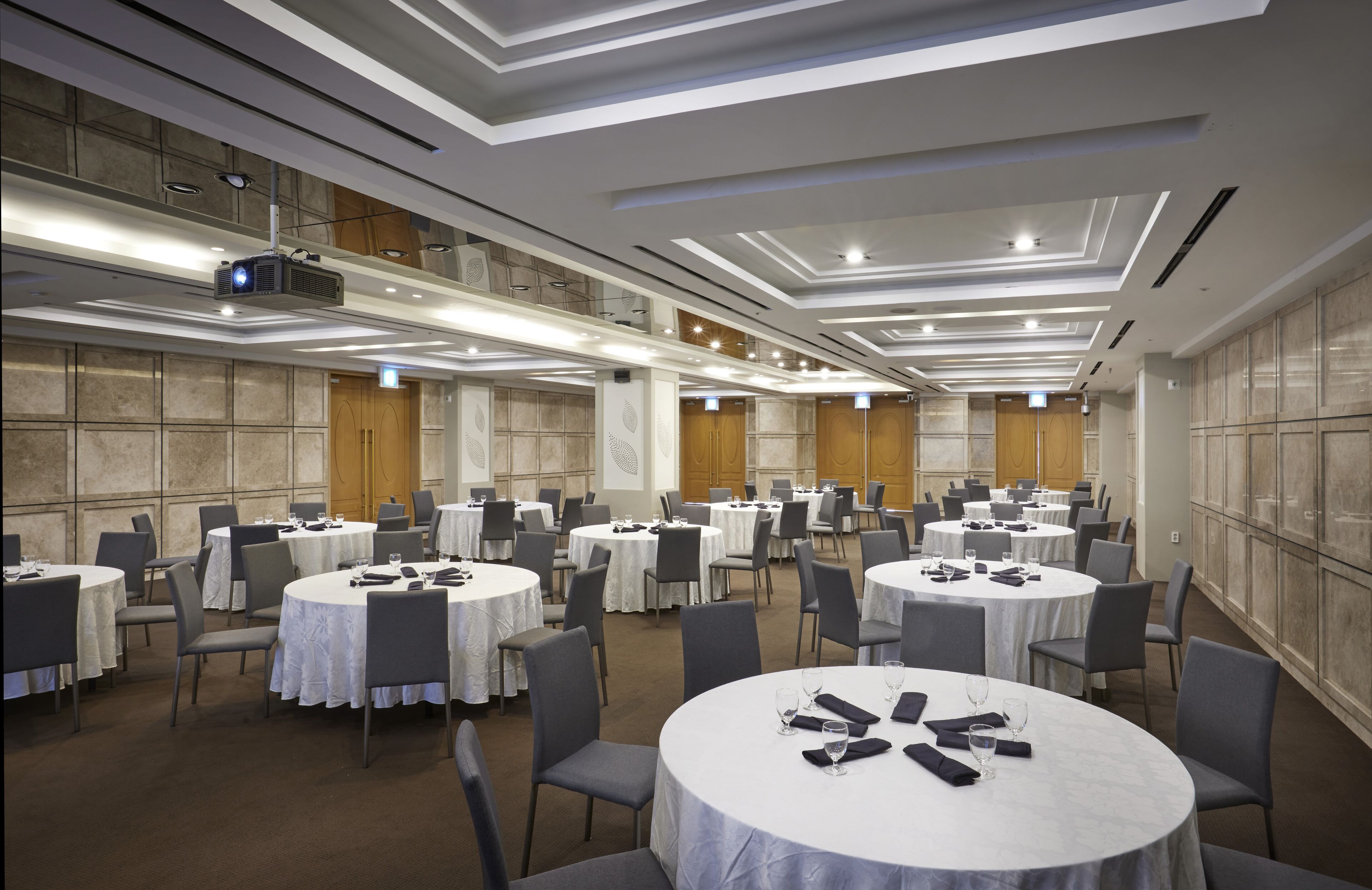 A conference room with multiple round tables, each with chairs, and a projector on the ceiling.