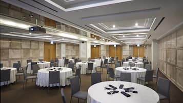 A conference room with multiple round tables, each with chairs, and a projector on the ceiling.