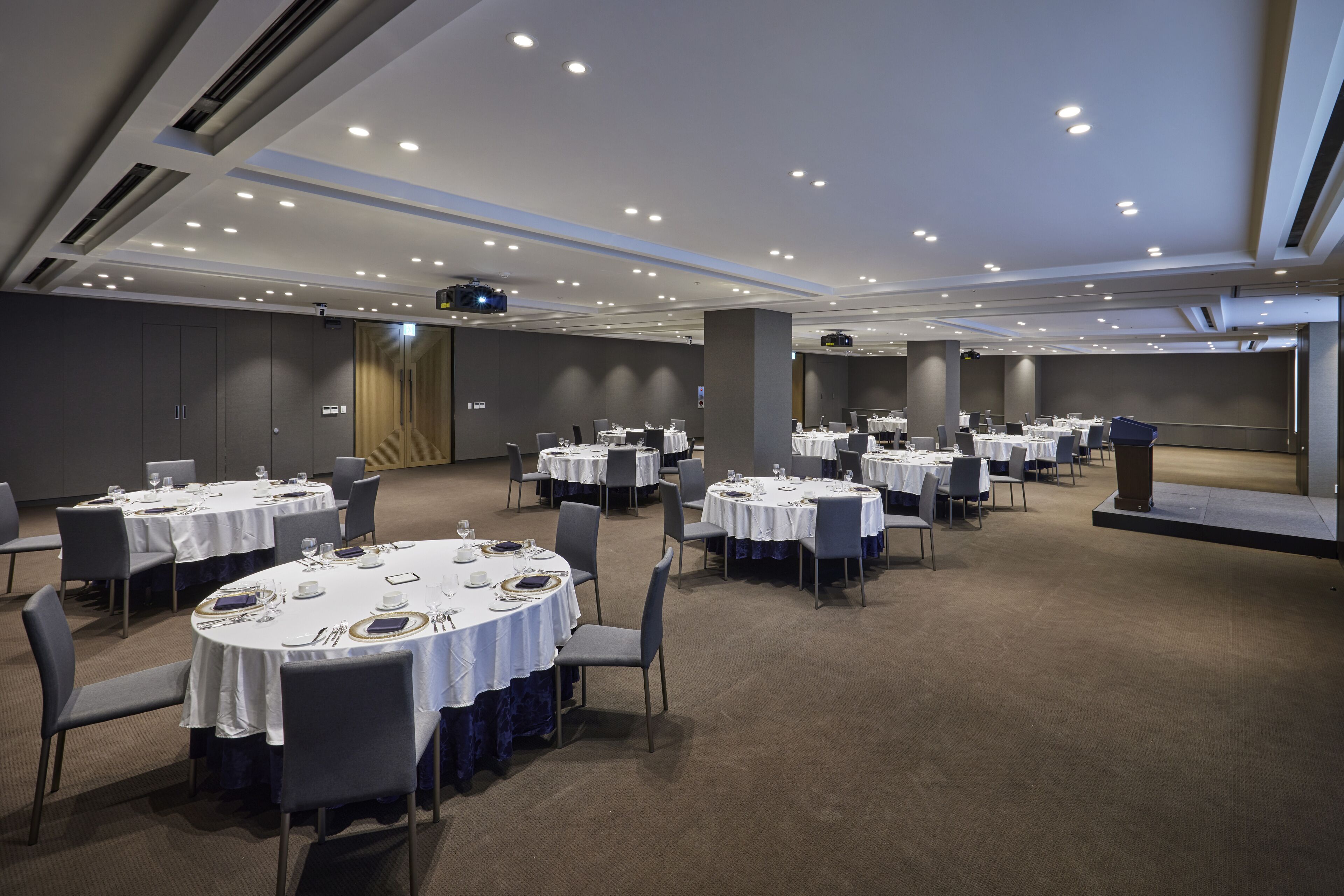 A conference room with multiple round tables, chairs, and a stage with a podium.