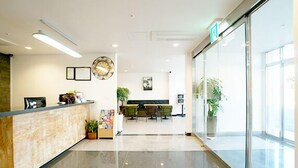 A reception area with a wooden reception desk, a clock, framed pictures, and a seating area with chairs and a table. - Marine Port Resort (Seogwipo)
