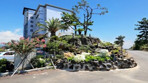 A building with a sign in a foreign language, surrounded by a landscaped garden with rocks, plants, and trees. - Marine Port Resort (Seogwipo)