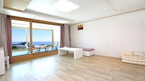 A modern living room with a large sliding glass door leading to a balcony with a view of the sea. - Marine Port Resort (Seogwipo)
