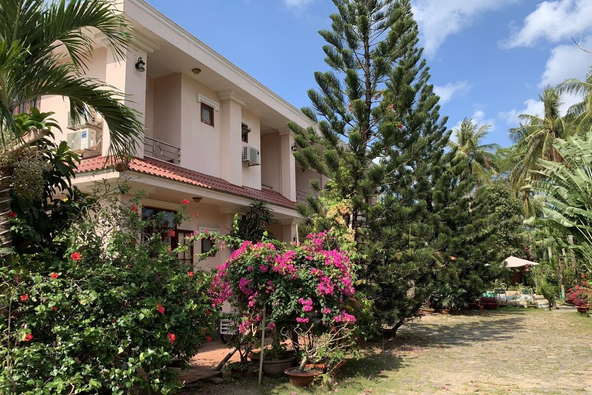 A two-story building with a balcony, surrounded by lush greenery and flowering plants.