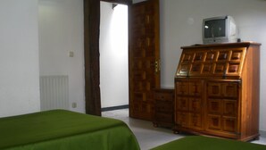 Una habitación con dos camas verdes, un aparador de madera con un televisor encima y una puerta que da a otra habitación.