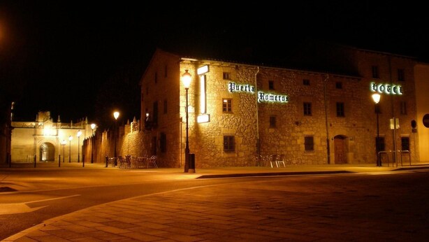 Un edificio de piedra con letreros iluminados que dicen "Puerta Romeros" y "HOTEL".