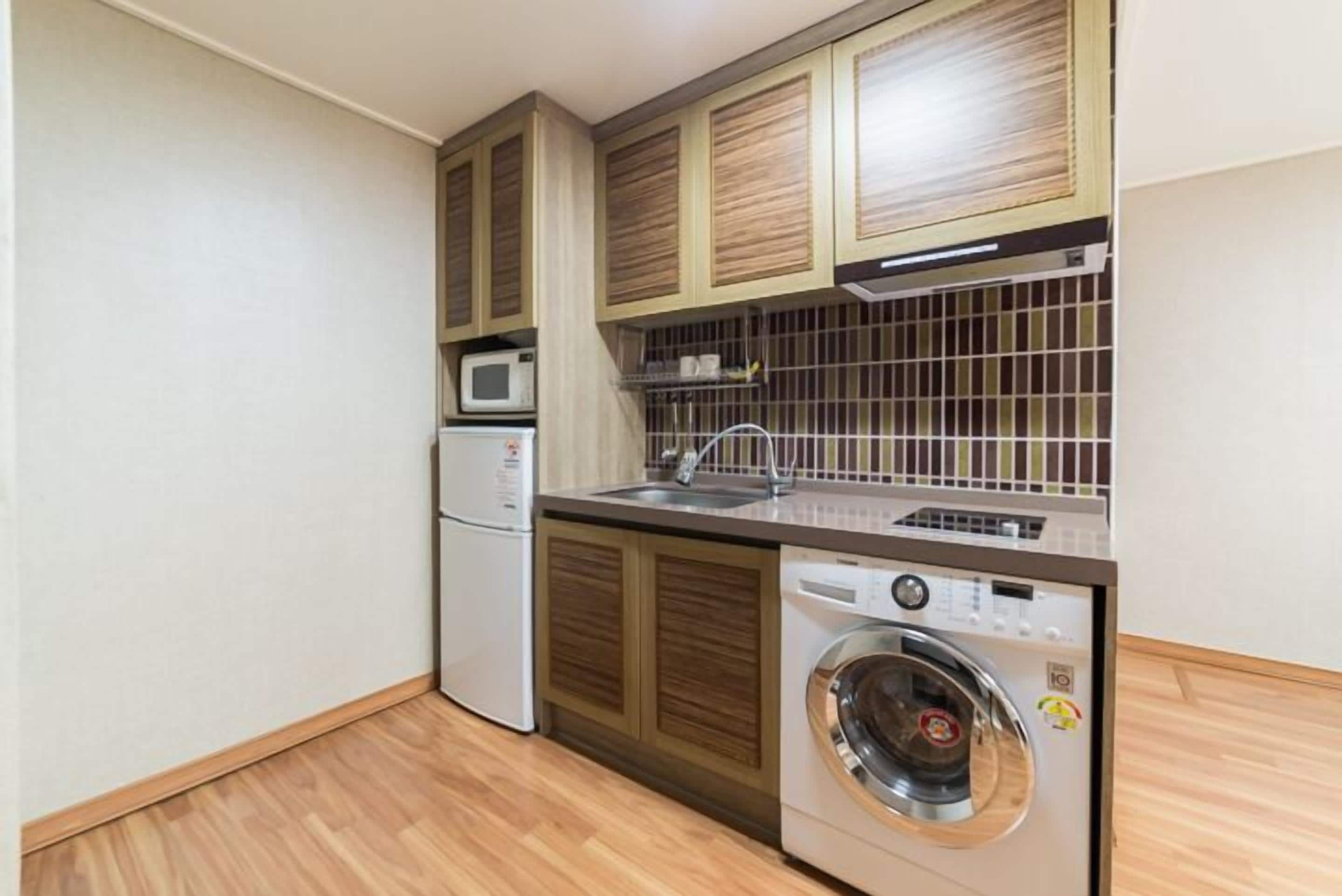 A compact kitchen with wooden cabinets, a microwave, a sink, and a front-loading washing machine.