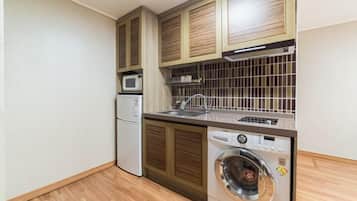 A compact kitchen with wooden cabinets, a microwave, a sink, and a front-loading washing machine.