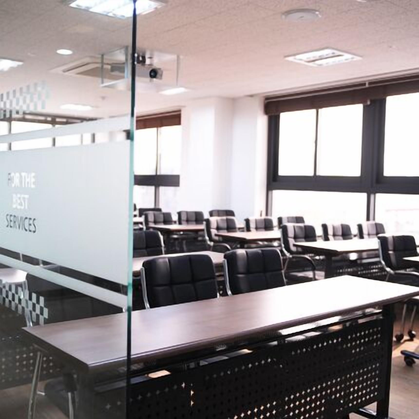 A conference room with a glass partition, black chairs, and tables.