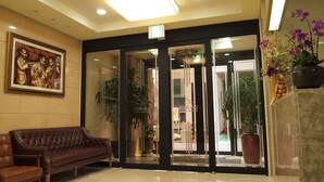 Un hall con un sofá de cuero marrón, un cuadro enmarcado y un mostrador de recepción con una planta en maceta.