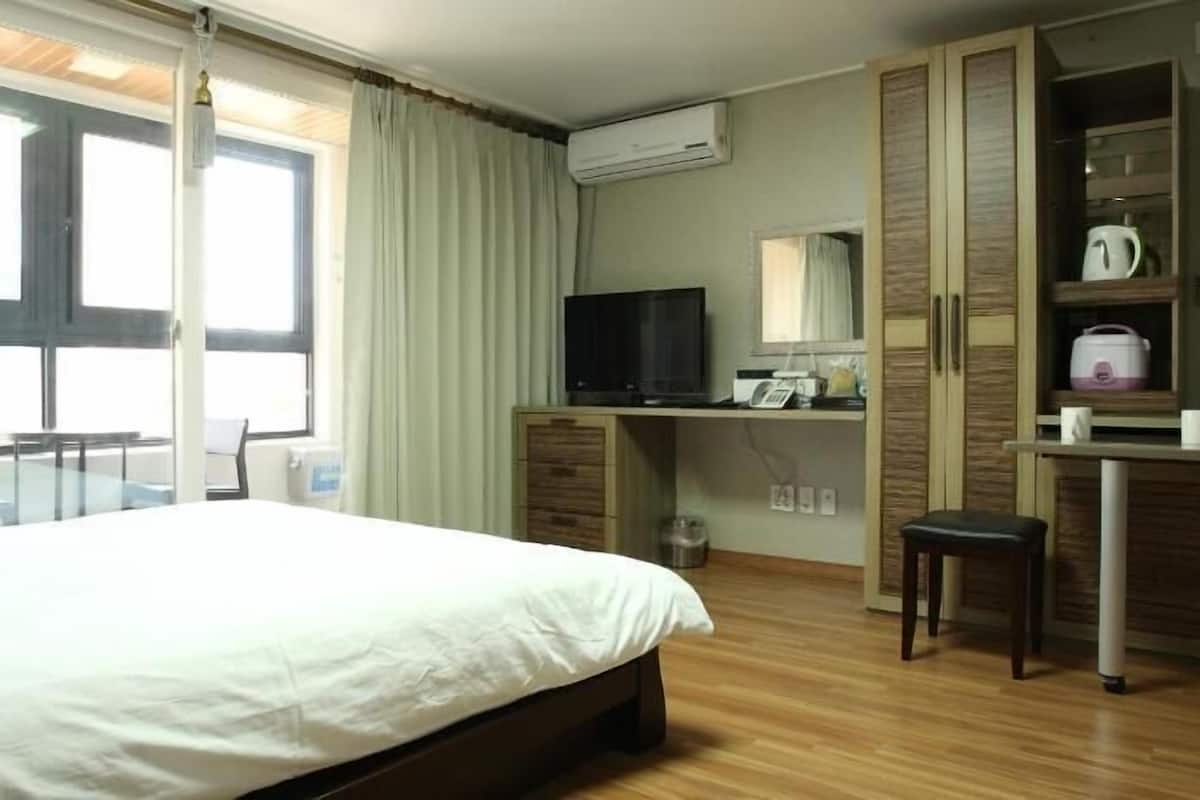 A hotel room with a bed, a desk with a TV, a kitchenette, and a window with curtains.