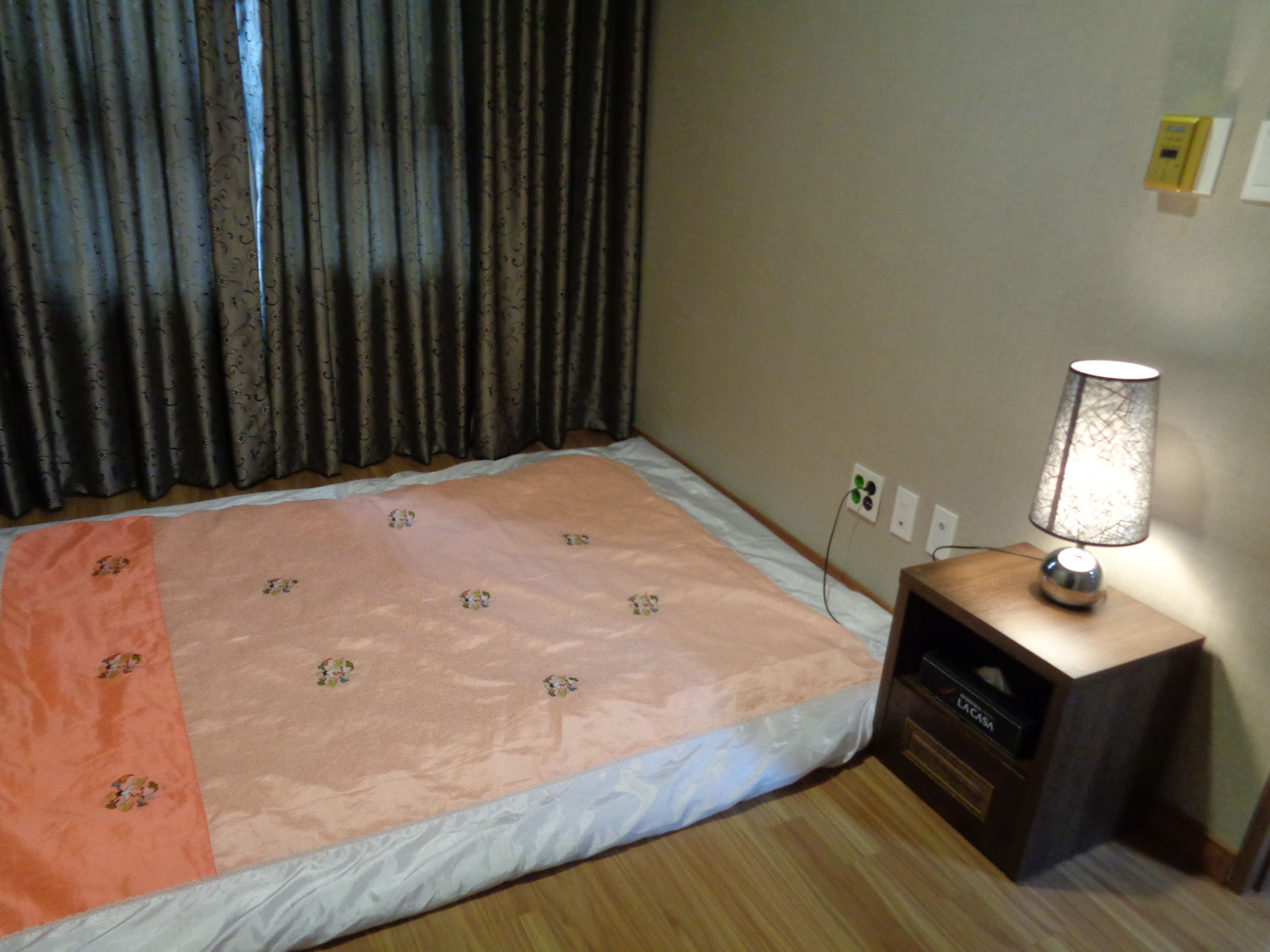 Ein Schlafzimmer mit einem Bett, einem Nachttisch, einer Lampe und einer Steckdose.