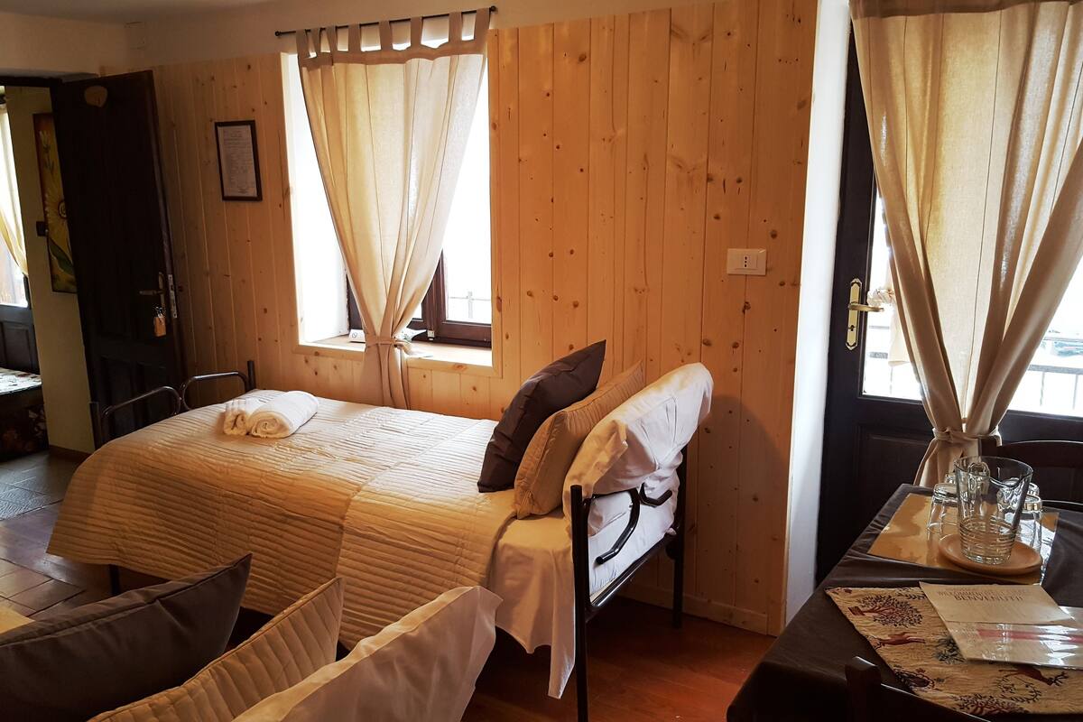 A cozy room with a bed, a table with a glass, and a window with curtains.