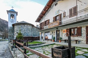 A traditional stone building with a bell tower, a signboard for 'Locanda Aquilabianca', and a wooden fence in front. - Locanda Aquila Bianca (Valprato Soana)