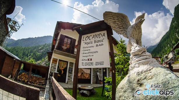 A sign for Locanda "Aquila Bianca" with a rustic stone building, a balcony, and a mountain backdrop. - Locanda Aquila Bianca (Valprato Soana)