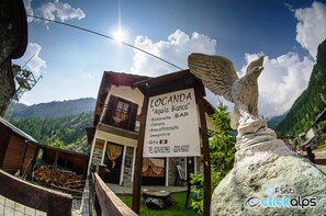 Une enseigne pour la « Locanda Aquila Bianca », avec un bâtiment en pierre au style rustique, un balcon et une vue sur les montagnes en arrière-plan.