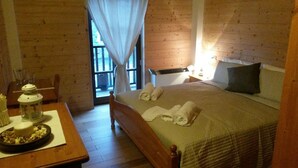 A wooden-paneled room with a bed, a table with a lantern, and a window with curtains. - Locanda Aquila Bianca (Valprato Soana)
