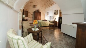 Una sala de estar acogedora con un sofá, una mesa de madera con un florero, y una zona de cocina con un refrigerador y una mesa de comedor.