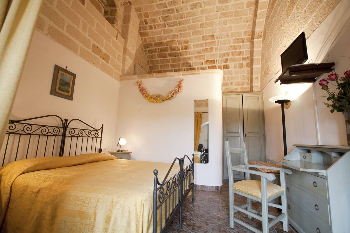 A bedroom with a brick ceiling, a bed with a headboard, a chair, a dresser, and a mirror.