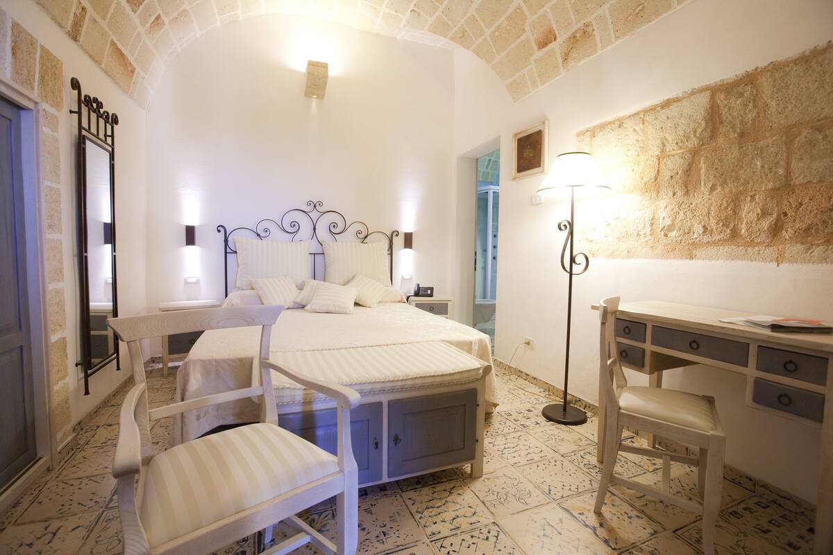 A bedroom with a bed, two chairs, a desk, and a lamp.