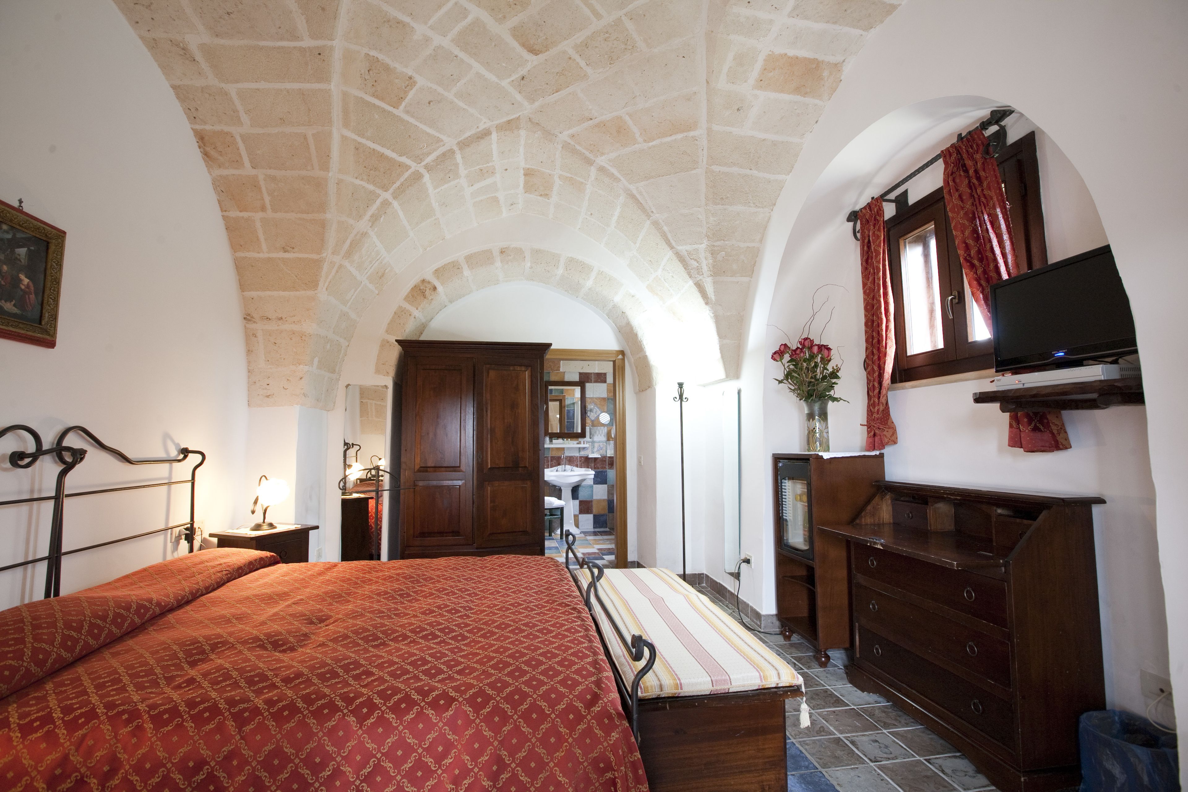 Quarto com cama, cómoda de madeira, televisão e teto de pedra em arco.