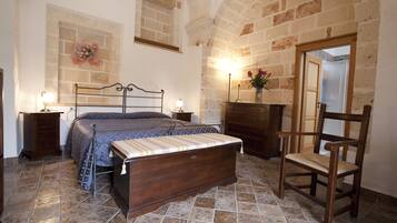 Un dormitorio con cama, mesitas de noche, una silla de madera, cómoda y pared de piedra.