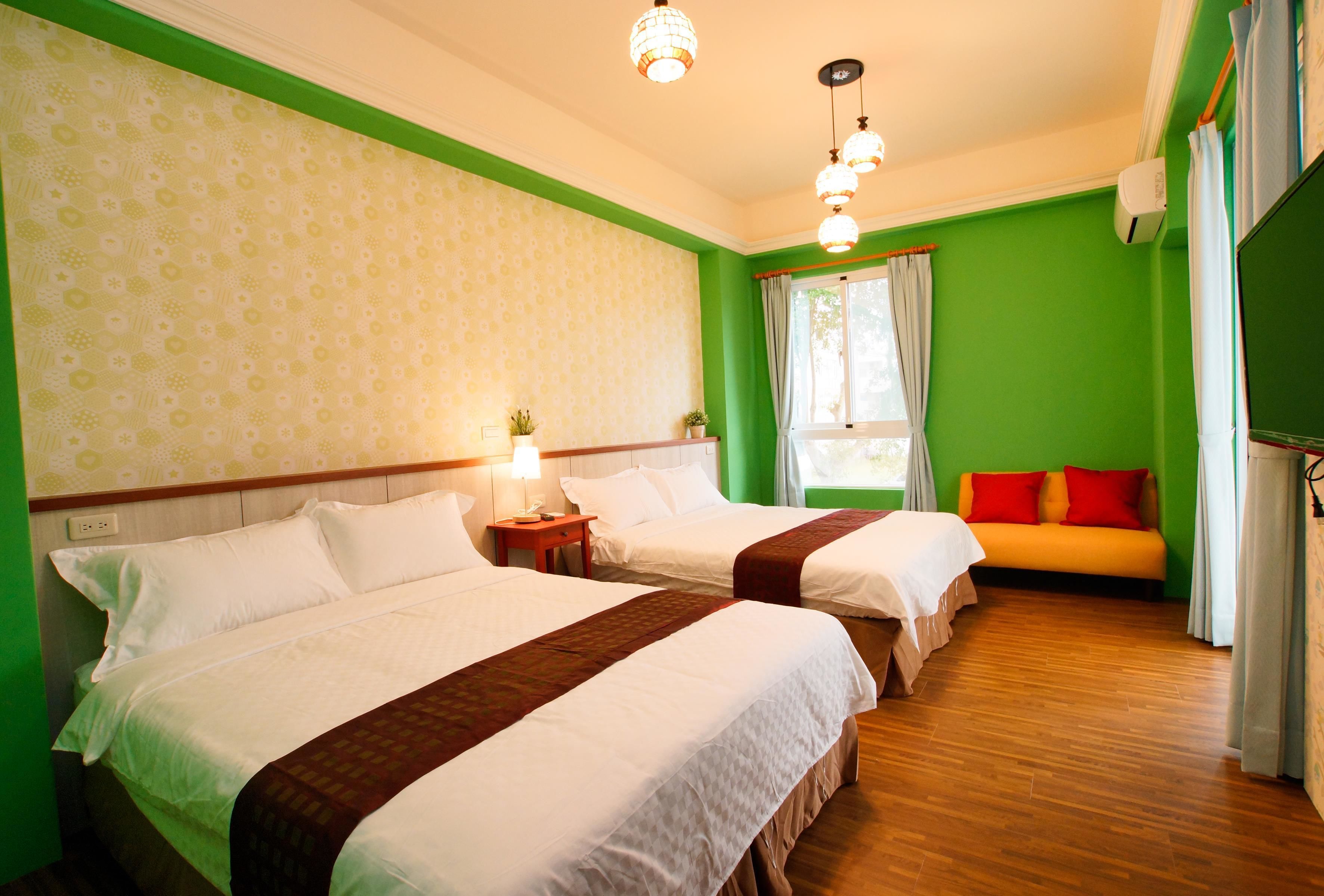 A hotel room with two beds, a sofa, a window with curtains, and a ceiling light fixture.