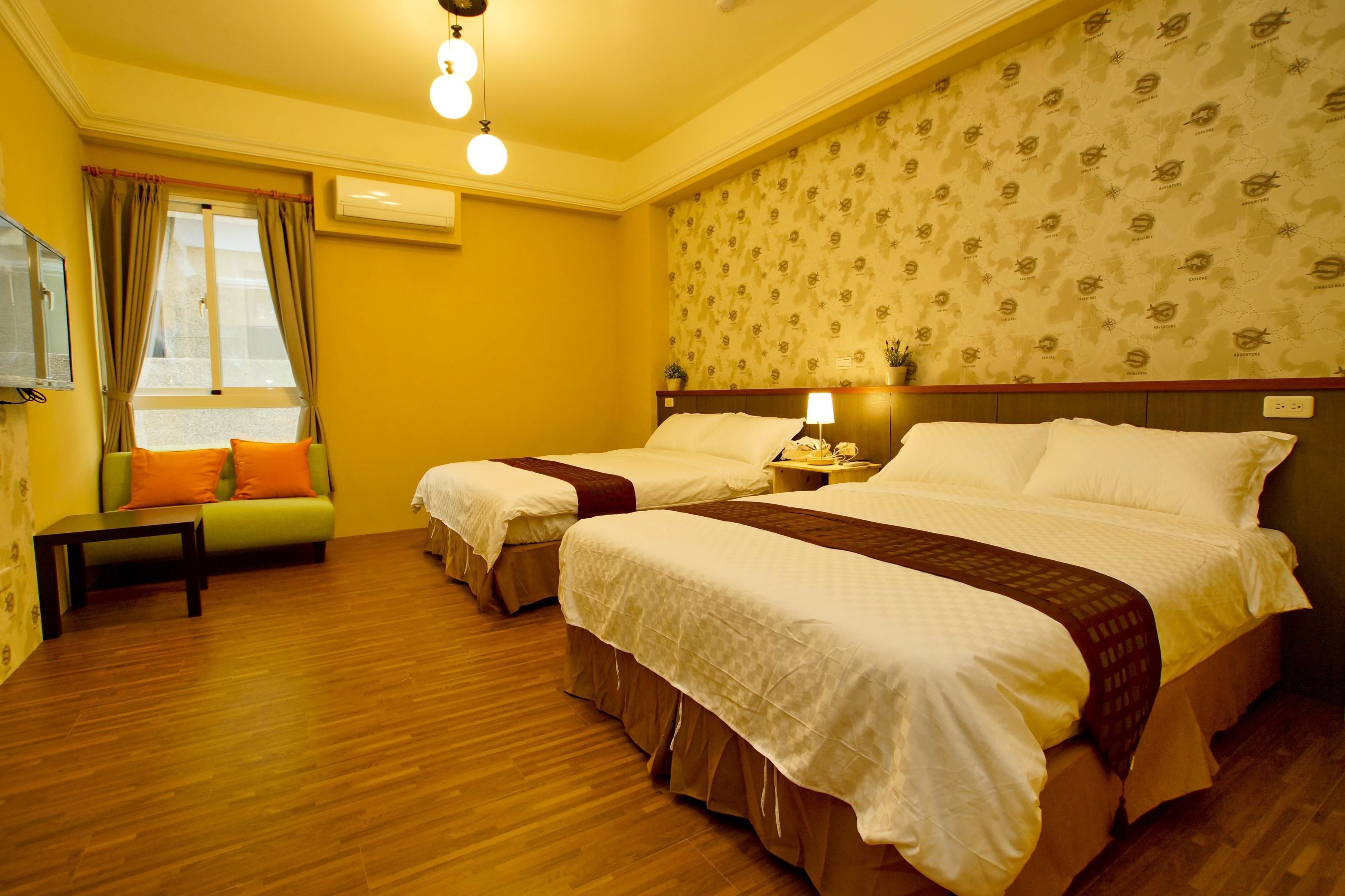 A hotel room with two beds, a sofa, a small table, and a window with curtains.