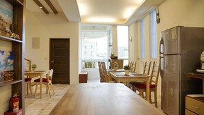A spacious kitchen with a long wooden table, chairs, a refrigerator, and a window with a city view. - Soft Travel Hostel (Taitung)