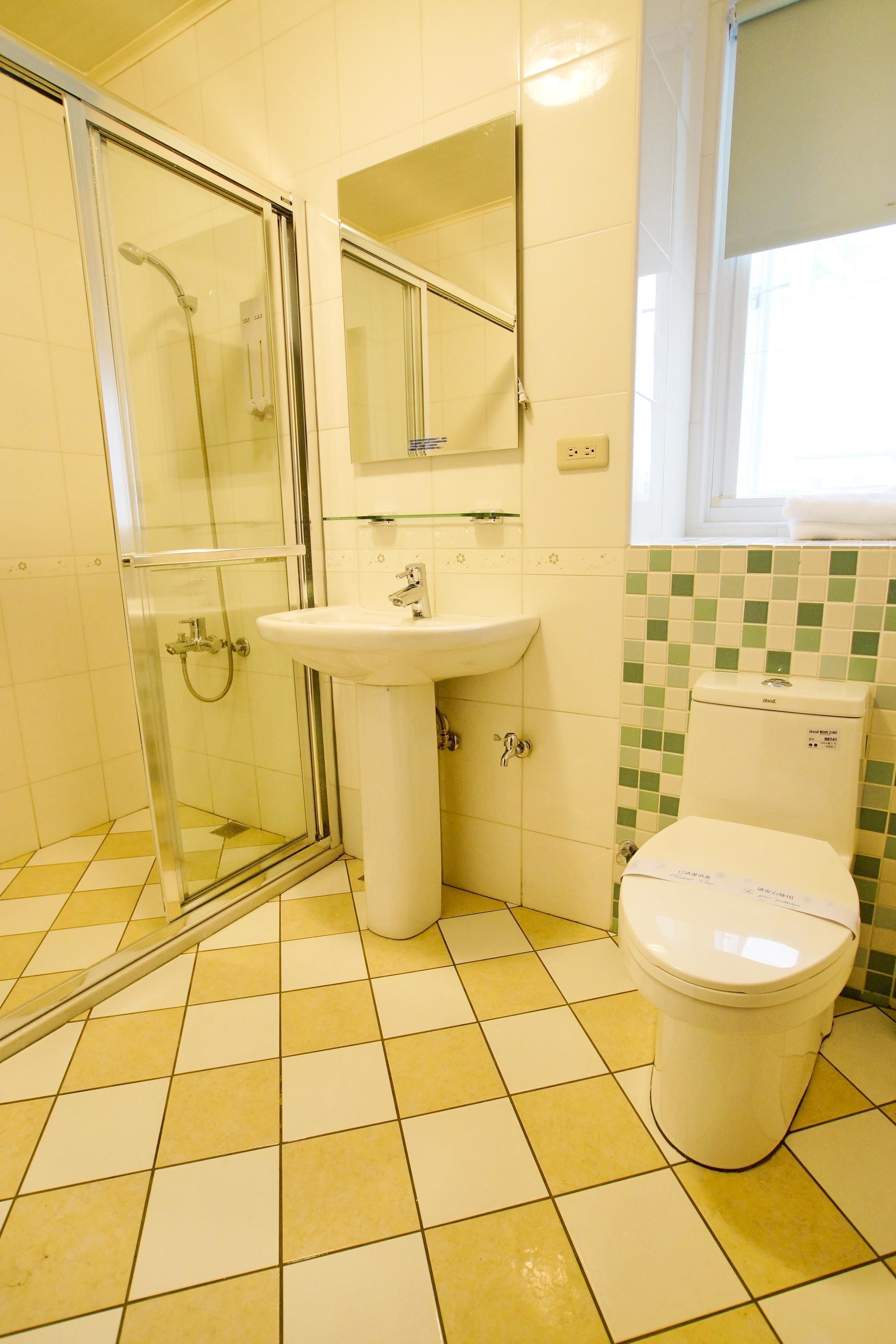 A bathroom with a glass shower enclosure, a sink, a toilet, and a window.