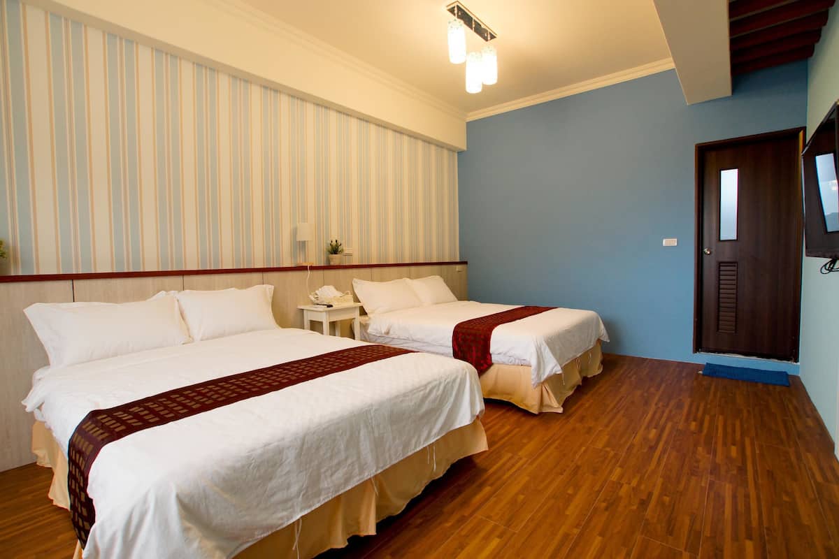 A hotel room with two beds, wooden flooring, a striped wall, a small table with a phone, and a door with a mirror.