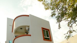 A modern two-story building with a curved facade, a small balcony, and a wooden deck with outdoor seating. - Soft Travel Hostel (Taitung)