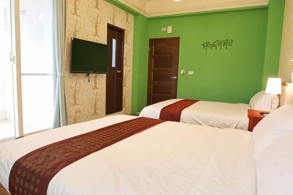 A hotel room with two beds, a TV, a door, and a green wall.