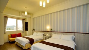 A hotel room with two beds, a sofa, a window with curtains, a bedside table with a lamp, and a wall-mounted shelf. - Soft Travel Hostel (Taitung)