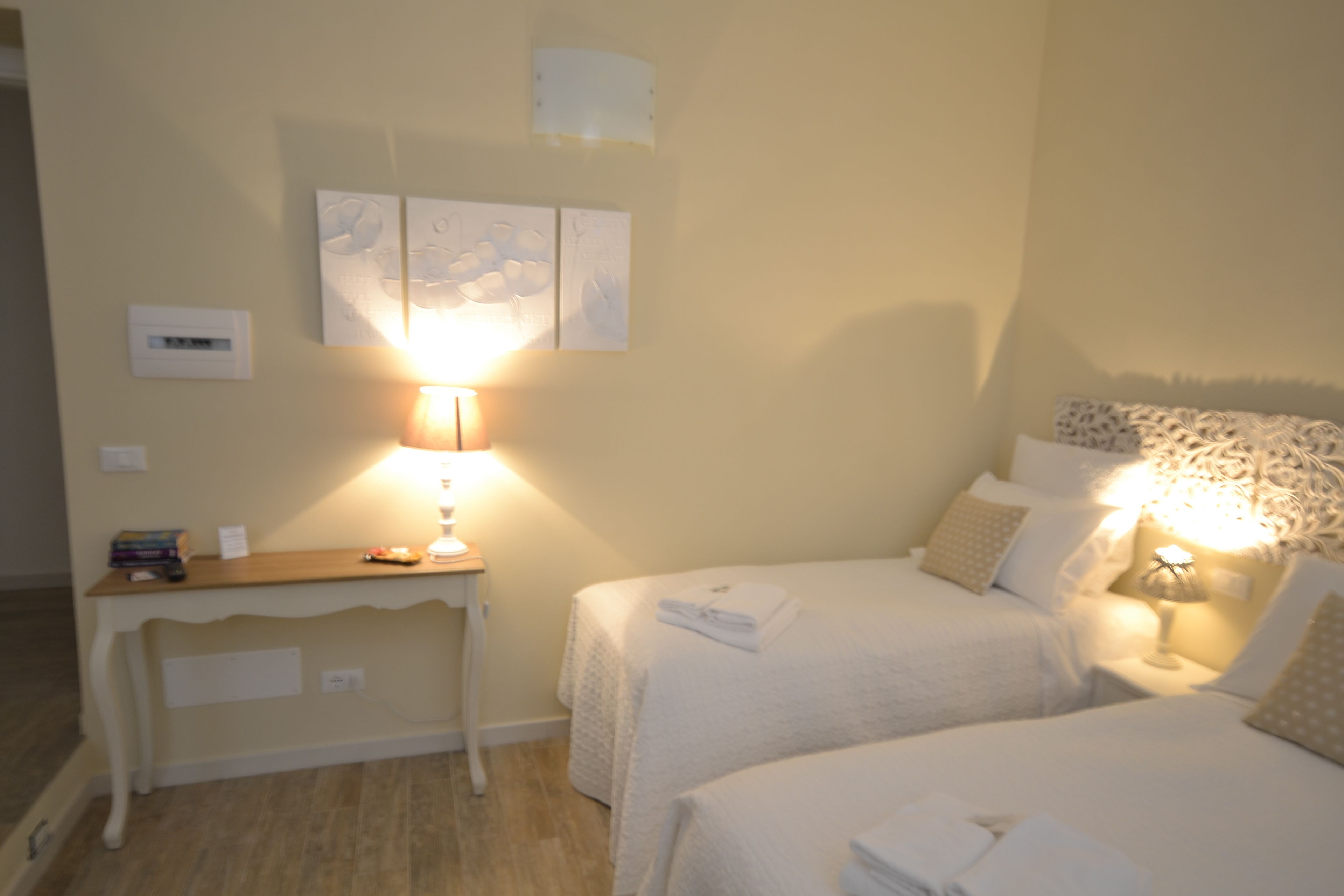 A hotel room with two beds, a bedside table, a lamp, and wall art.
