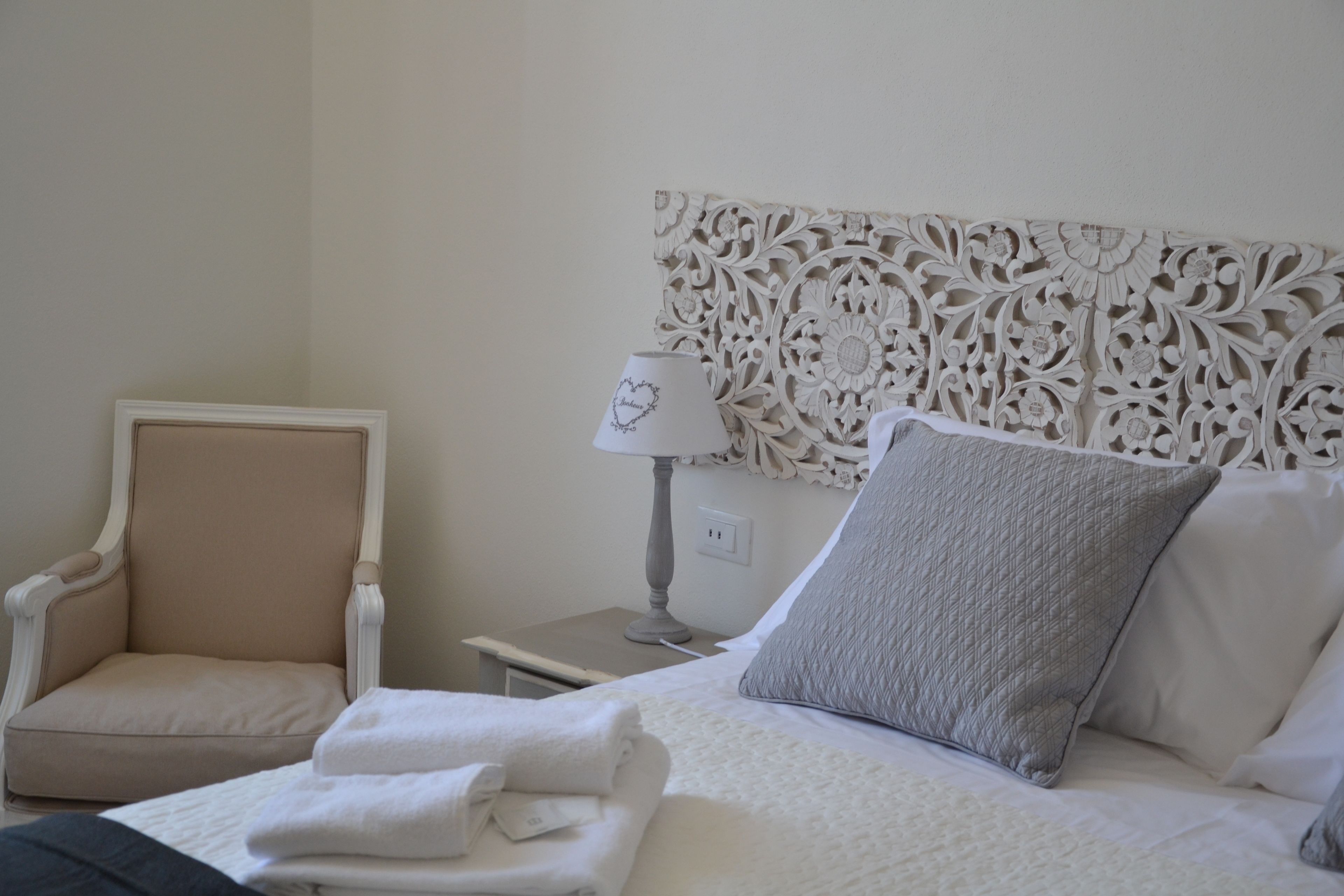 Habitación de hotel ordenada con cama, una silla, una mesita de noche y un cabecero decorativo.