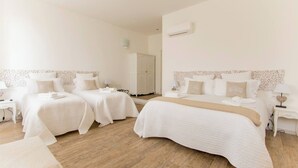Een hotelkamer met twee enkele bedden en een tweepersoonsbed, allemaal met witte beddengoed. Er is een garderobe en een nachtkastje met een lamp.