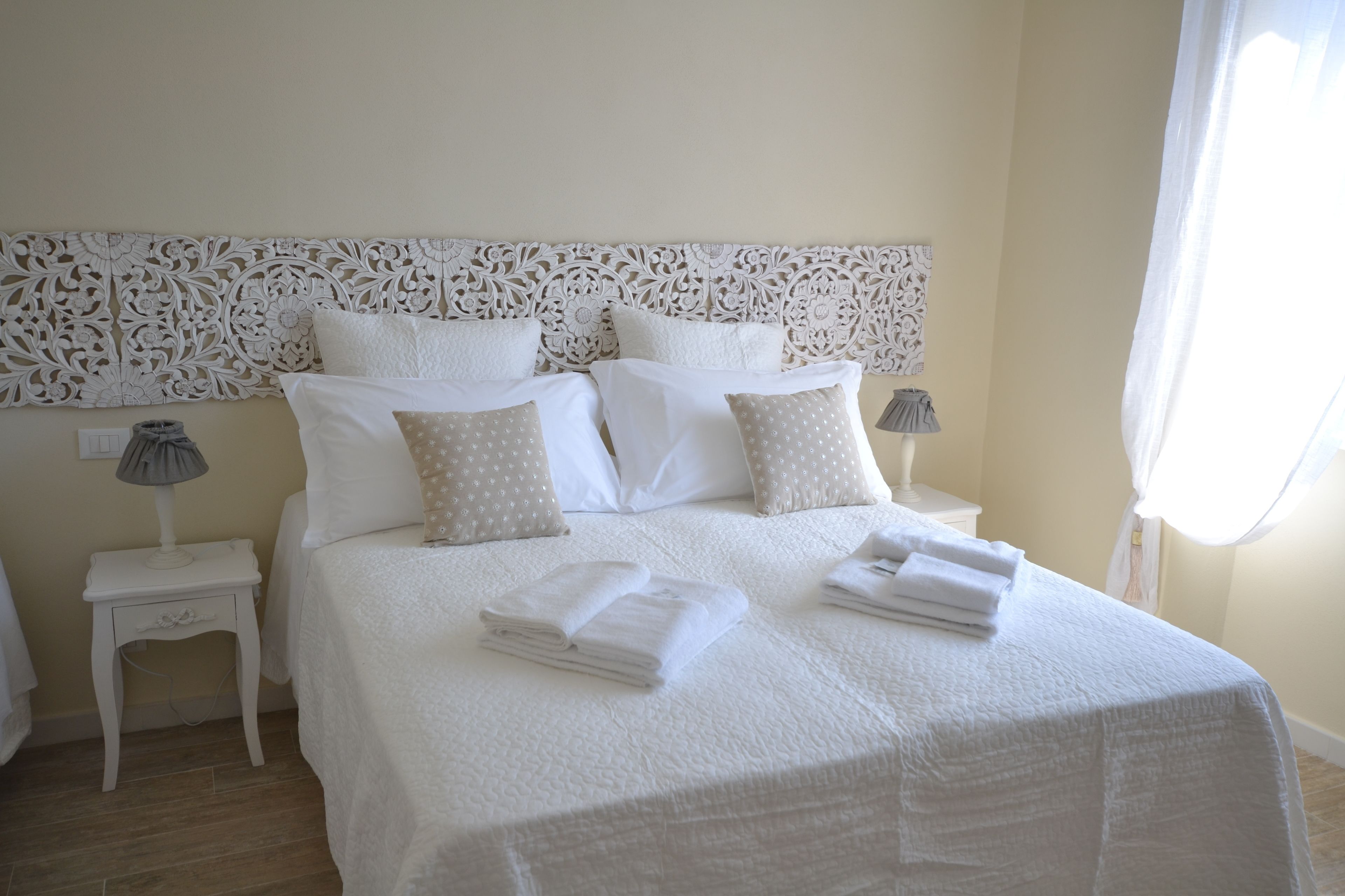 A neatly made bed with white bedding and folded towels, a decorative headboard, and bedside lamps.