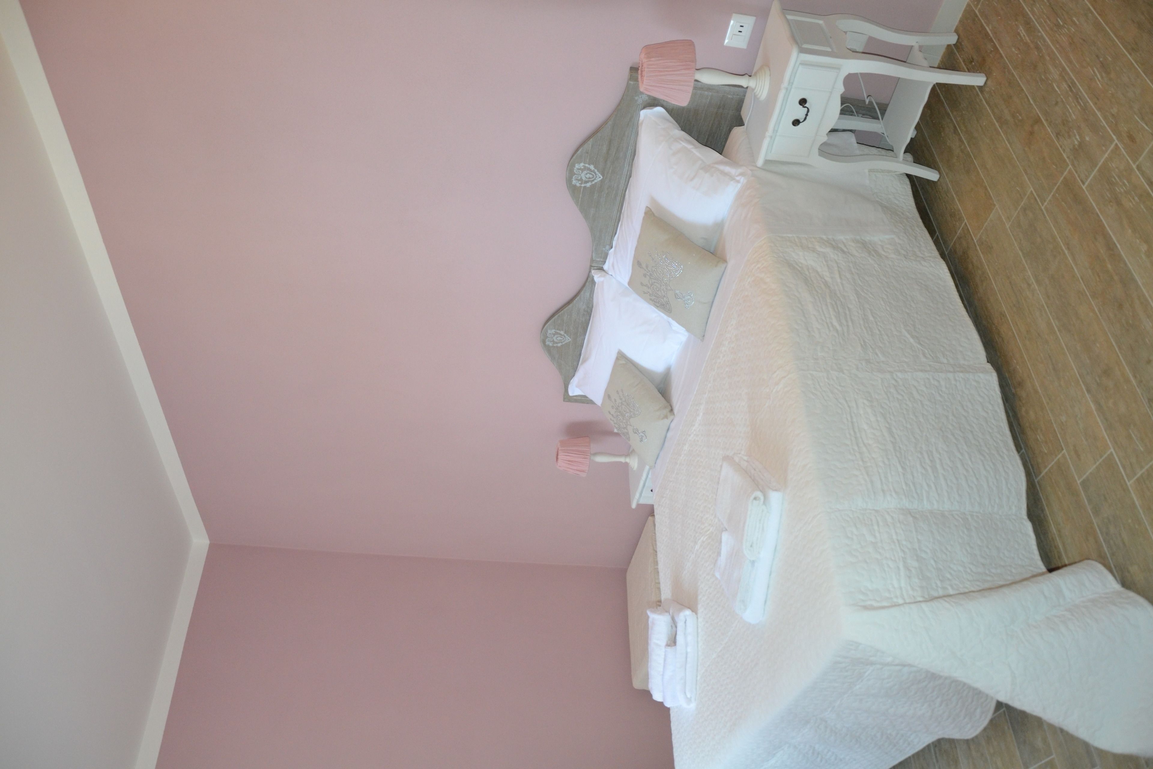 Een hotelkamer met een roze muur, een wit bed met een witte spreidek en een houten vloer.