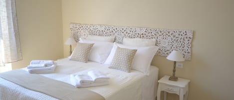 Una cama bien hecha con sábanas y almohadas blancas, una mesita de noche con lámpara y un cabecero decorativo.