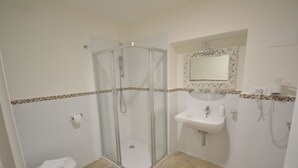 Een badkamer met een douche met glazen wand, een toilet, een wastafel en een spiegel met decoratieve lijst.