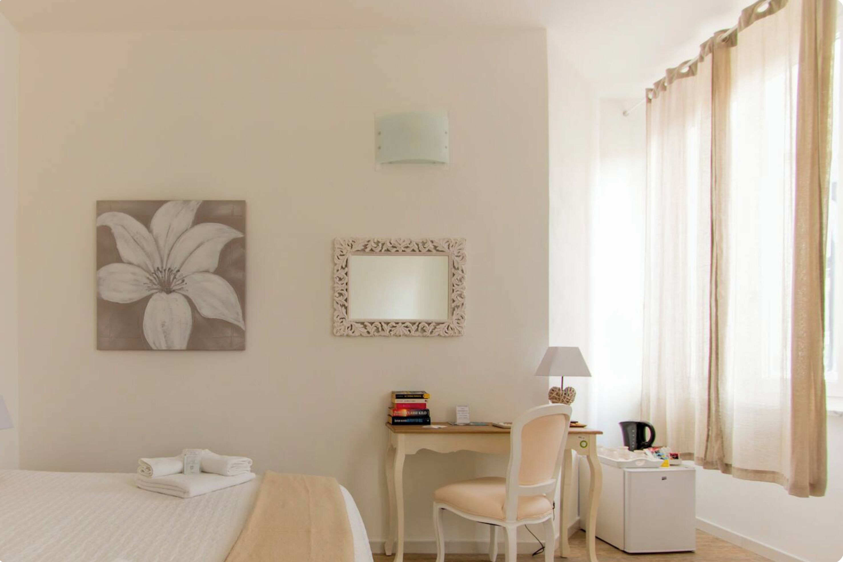 A hotel room with a bed, a desk, a chair, a small refrigerator, a lamp, and a window with curtains.