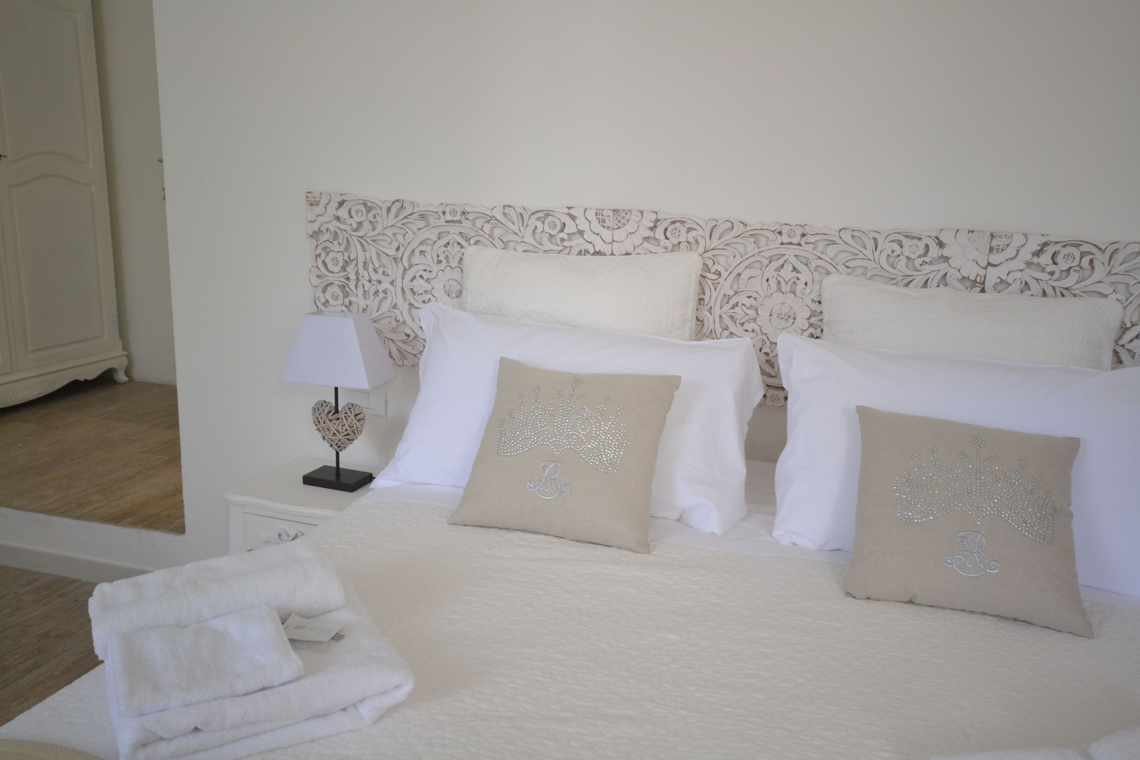 A neatly made bed with white linens and decorative pillows, a bedside table with a lamp, and a white wardrobe.