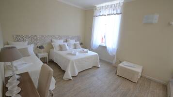 A hotel room with two beds, a small table with a lamp, a chair, and a window with curtains.