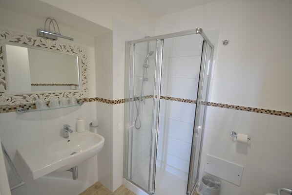 A bathroom with a glass-enclosed shower, a white sink, and a mirror with a decorative frame.