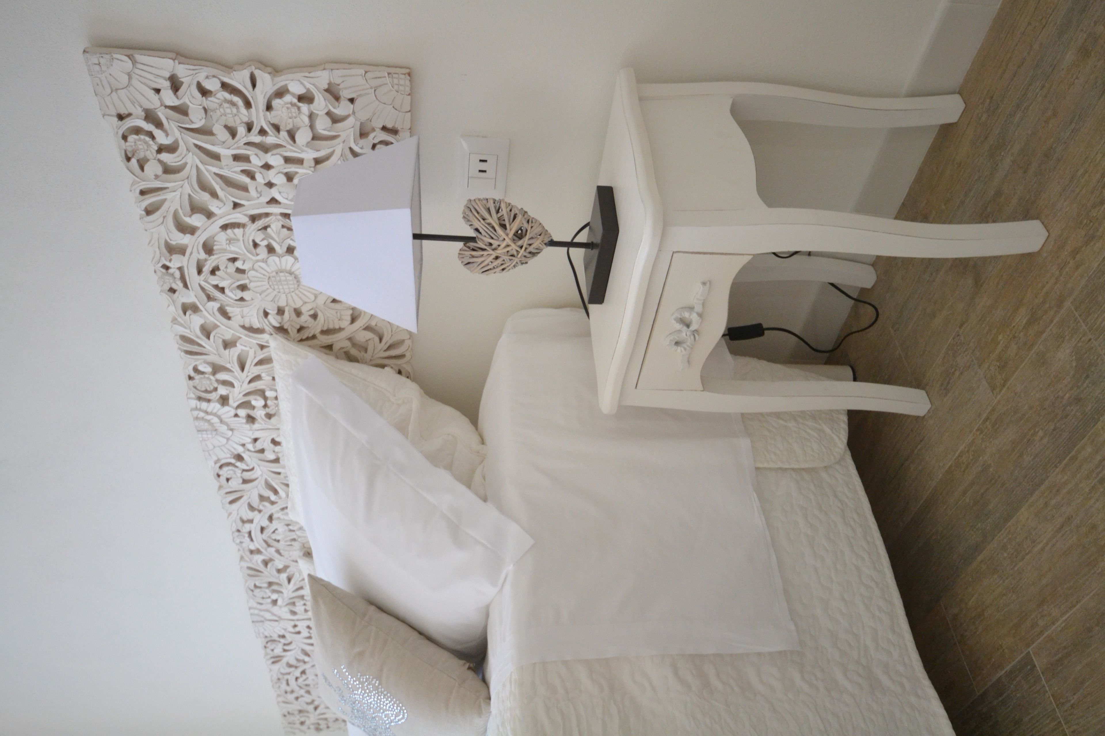 A room with a bed, a bedside table, a decorative wall piece, and a power outlet.