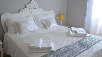 Een opgemaakt bed met witte lakens, een decoratief hoofdbord en een gevouwen handdoek ernaast.