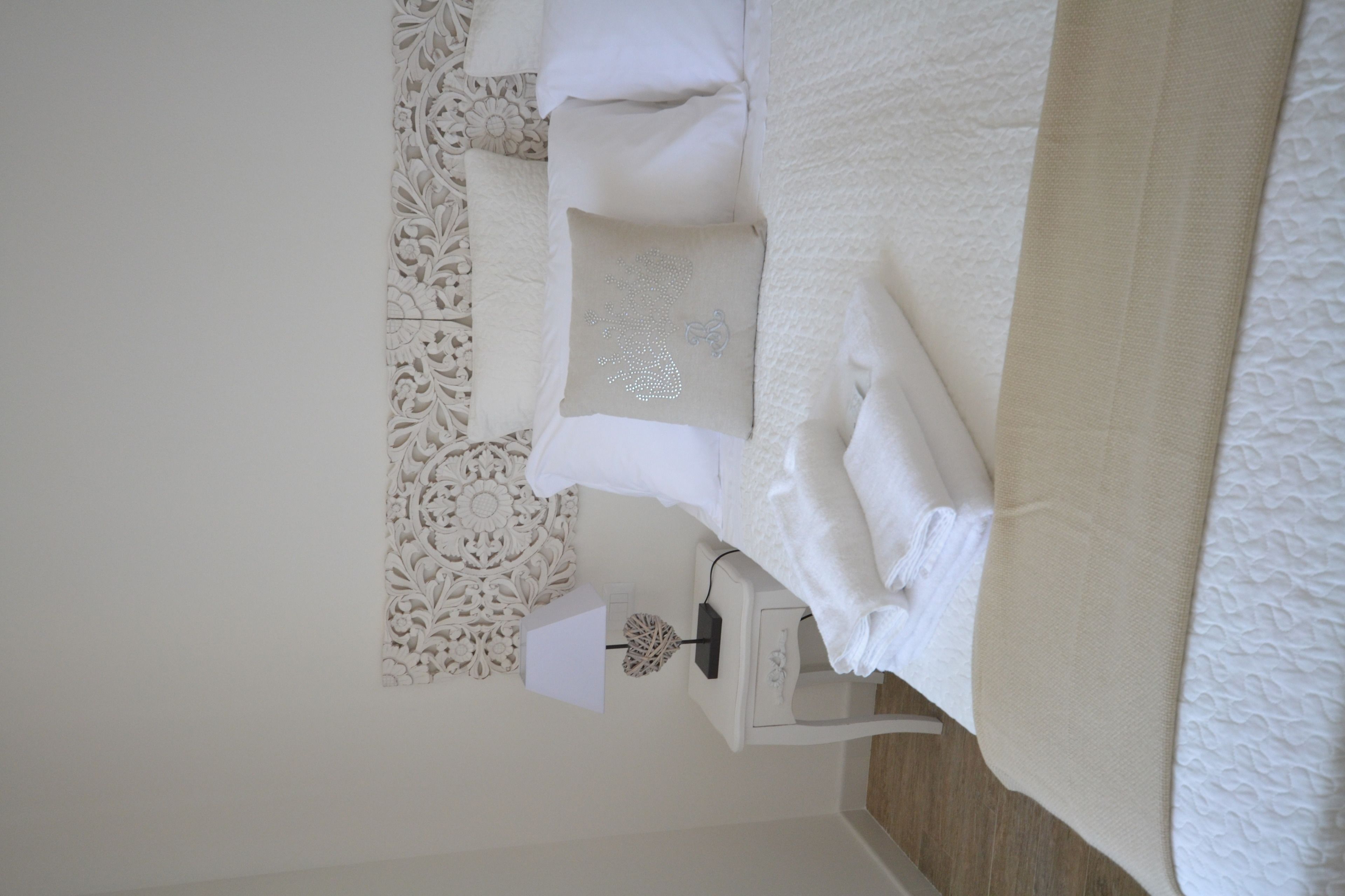 Una cama bien hecha con ropa de cama blanca y un cojín decorativo.