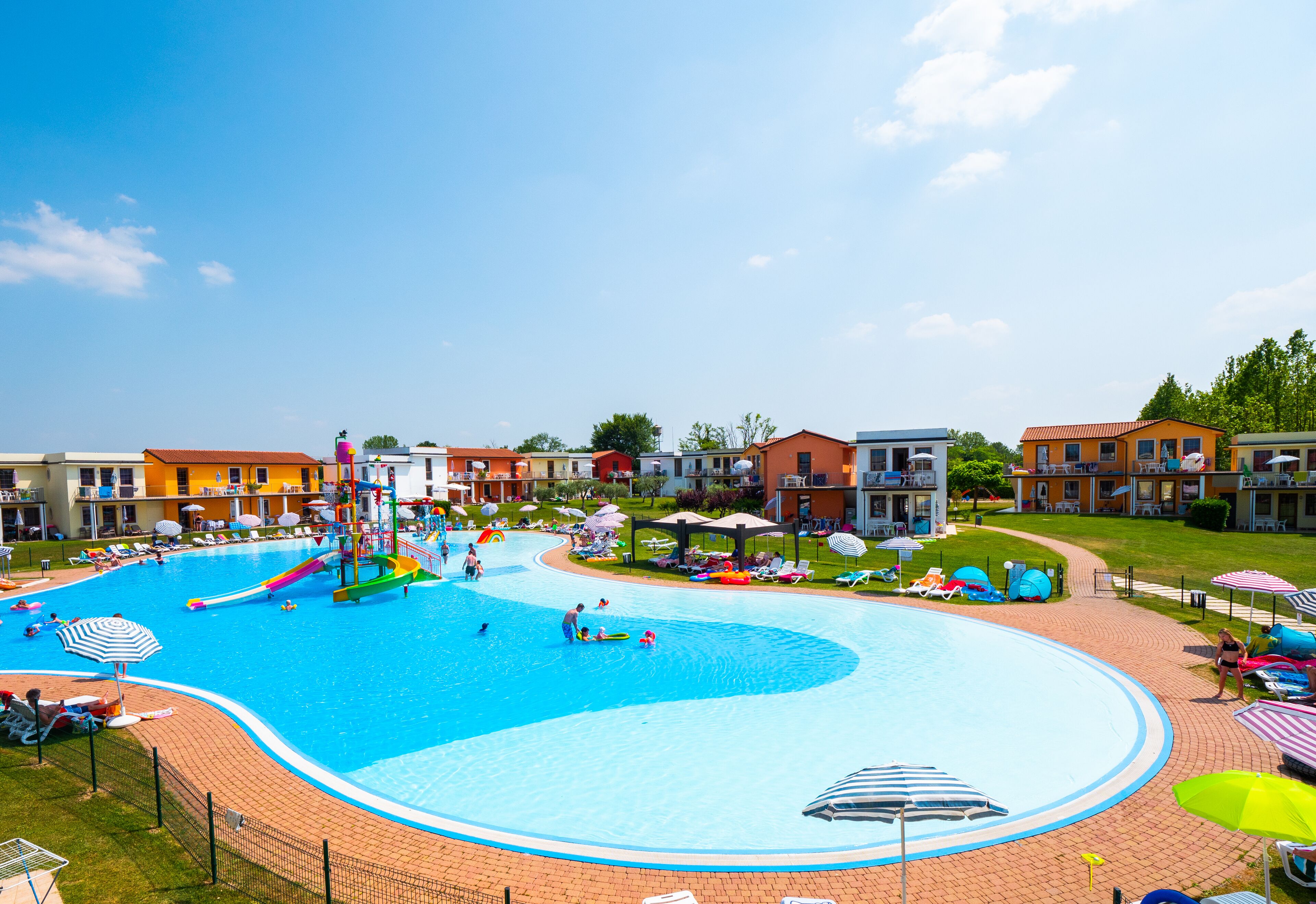 Une piscine avec un toboggan, entourée de chaises longues et de parasols, avec des bâtiments en arrière-plan.