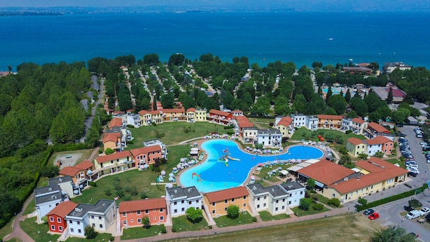 Vista aerea di una zona residenziale con una piscina centrale circondata da case con tetti rossi.