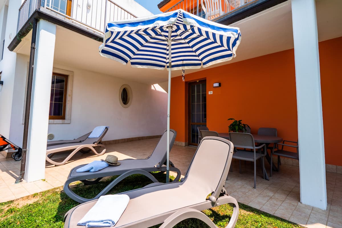 Un espace extérieur abrité, aménagé avec des fauteuils confortables et un parasol à rayures.